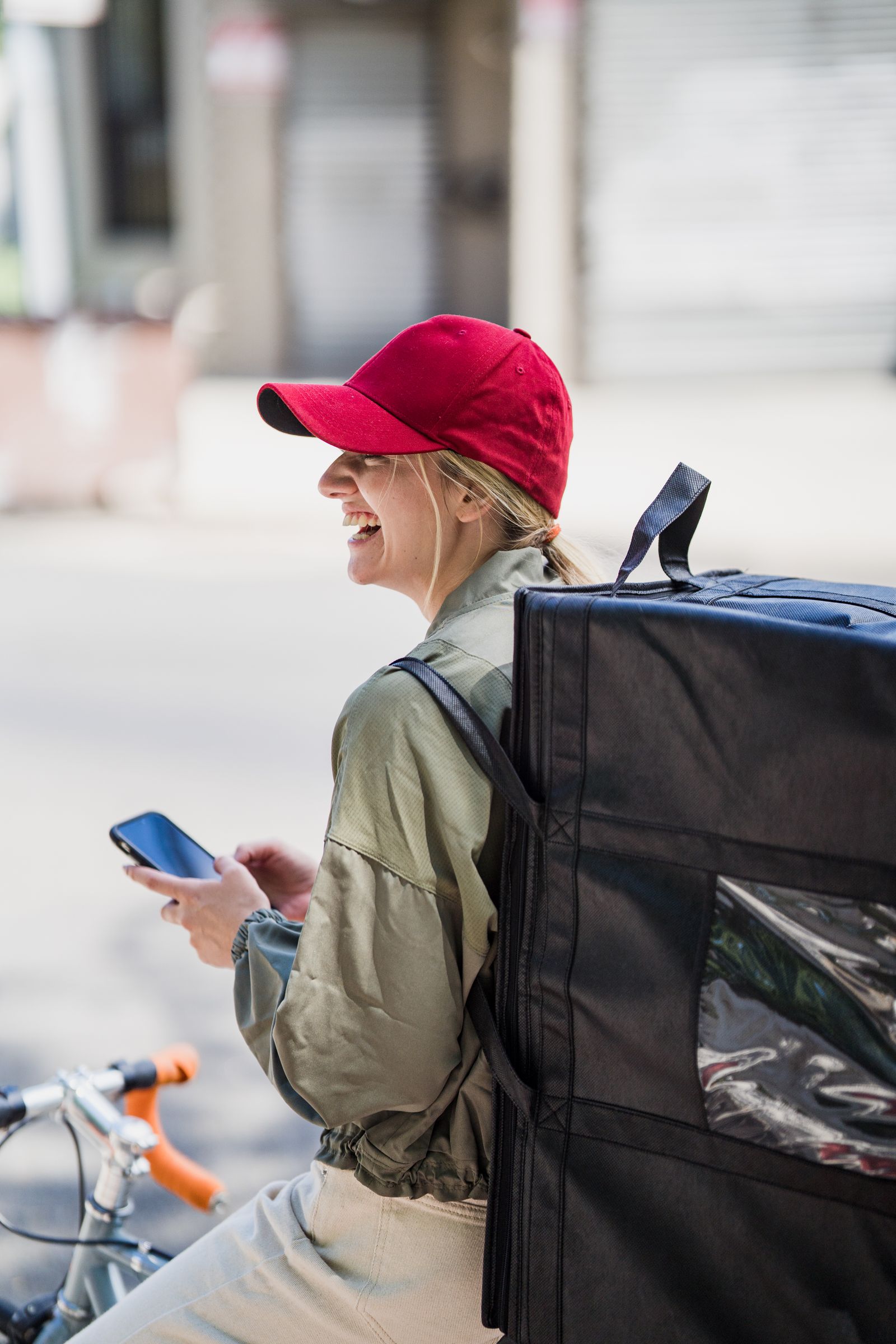 A courier checking her phone beside a bicycle while completing a delivery